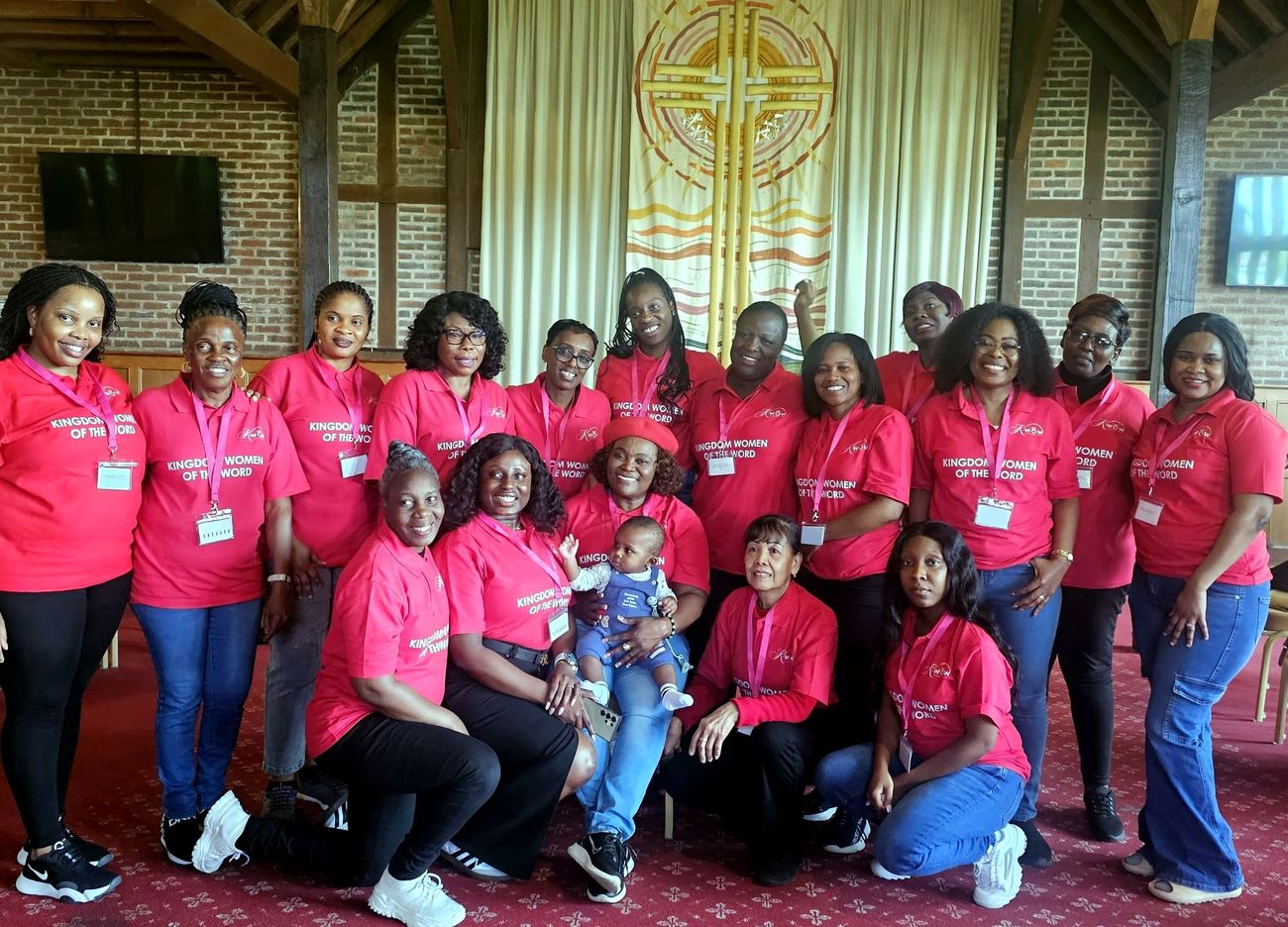 A large group of Kingdom Women of the Word gathered together before a woven cross